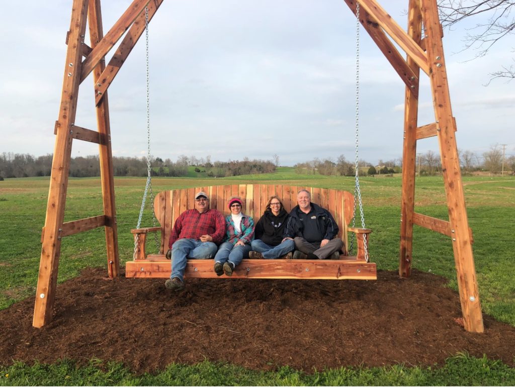 four people sitting on a large porch swing