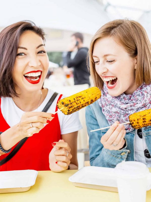 Woman friends eating street food corn at fastfood festival